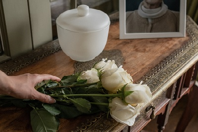 A hand placing white flowers next to an urn